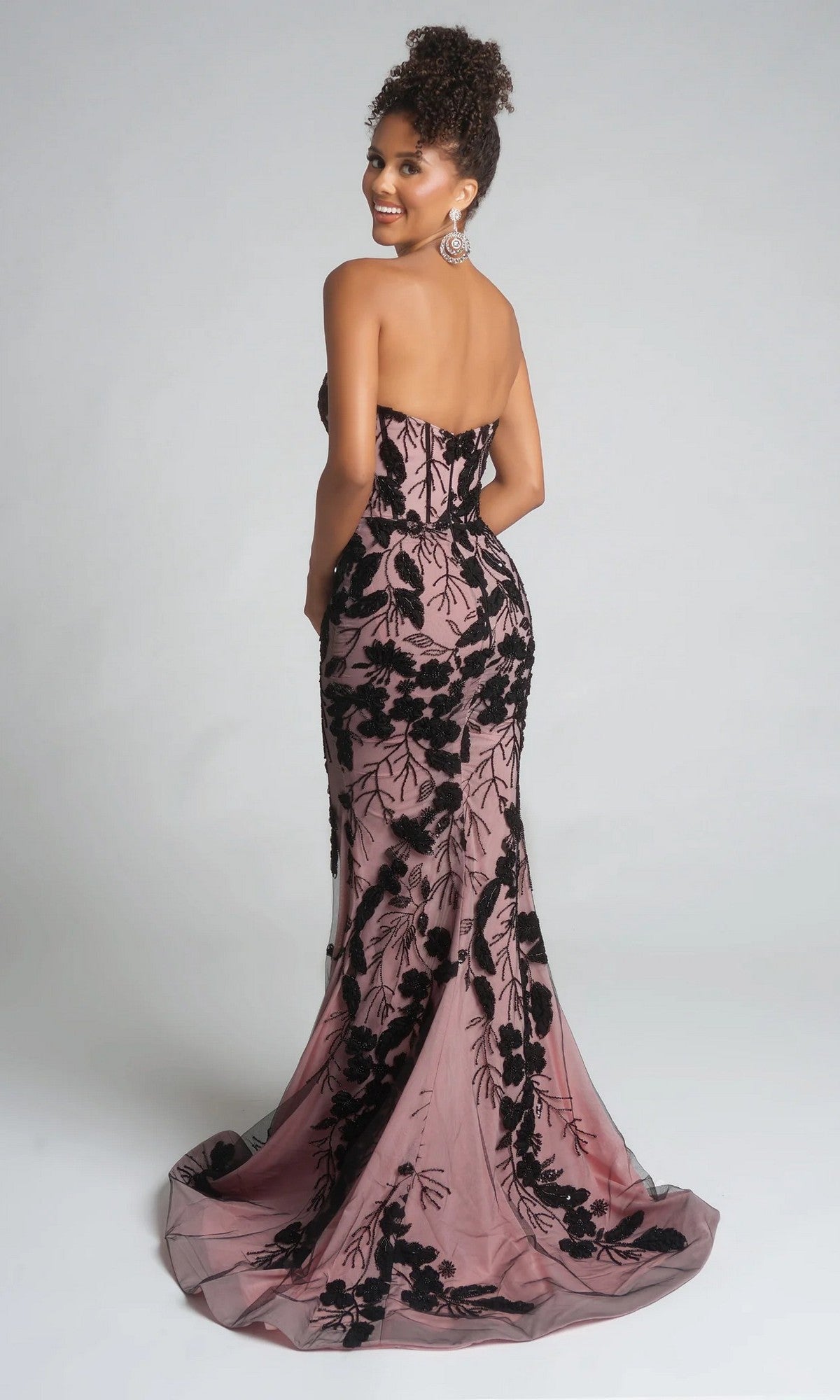 A woman poses with her back to the camera in the Portia and Scarlett PS26074 long formal dress, featuring a strapless sweetheart neckline, floor-length mauve fabric, black floral embroidery, and a subtle thigh-high slit.
